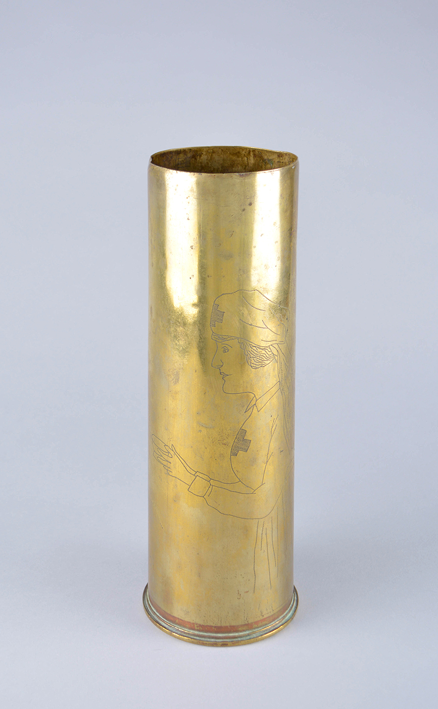 A vase made from a polished brass shell casing engraved with a detailed image of a nurse in full uniform.