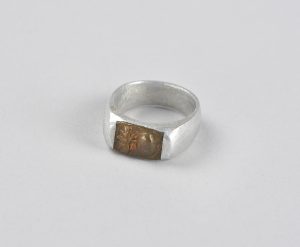 An aluminum ring with a brass top embossed with a flaming grenade.