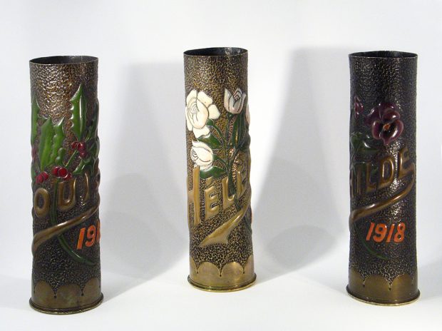 Three vases made from casings and embossed with plants, place names and dates. The plants and dates are painted colours.