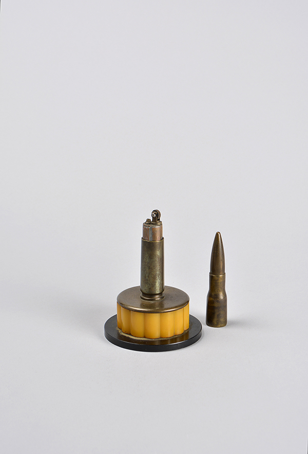 A bullet made into a lighter mounted on a brass and orange plastic bottom. The top of the bullet, which acts as the lid, is pulled off and set beside the lighter.
