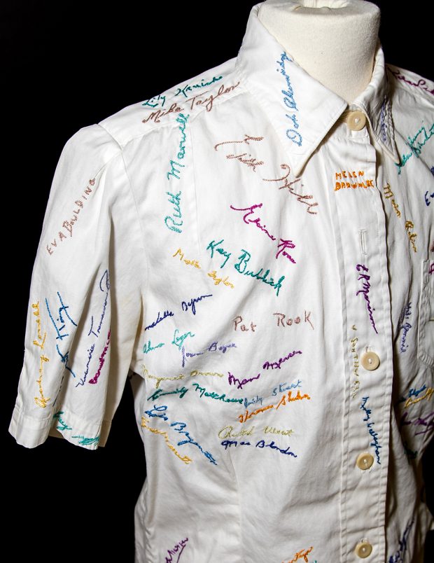 The front of a white collared shirt embroidered with signatures in various colors of thread.