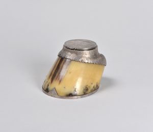 A horse’s hoof with finished silver forms at both ends. The silver is shaped like the lowest part of the horse’s leg at the top of the hoof and has a lid opening into an ink well.