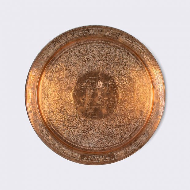 A larger shiny copper plate engraved with circles of design with a map in the middle.