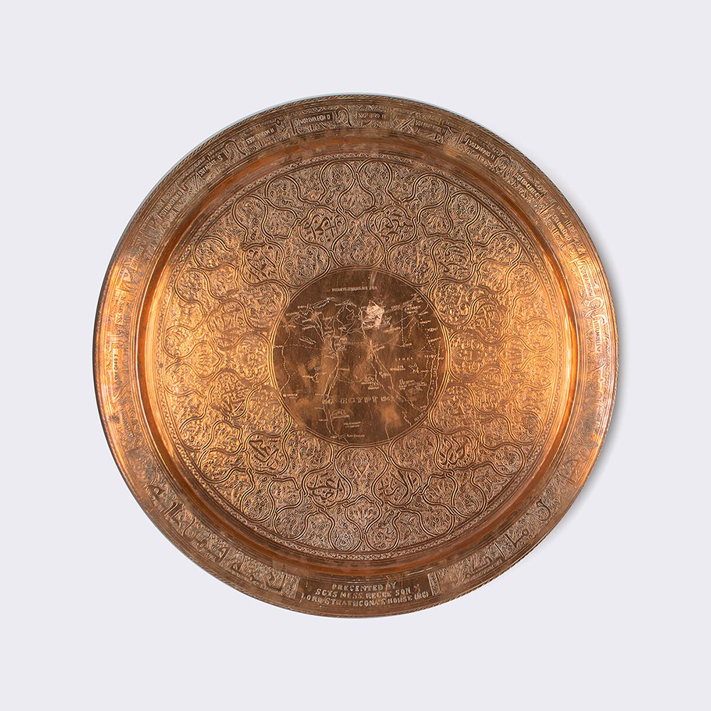 A larger shiny copper plate engraved with circles of design with a map in the middle.