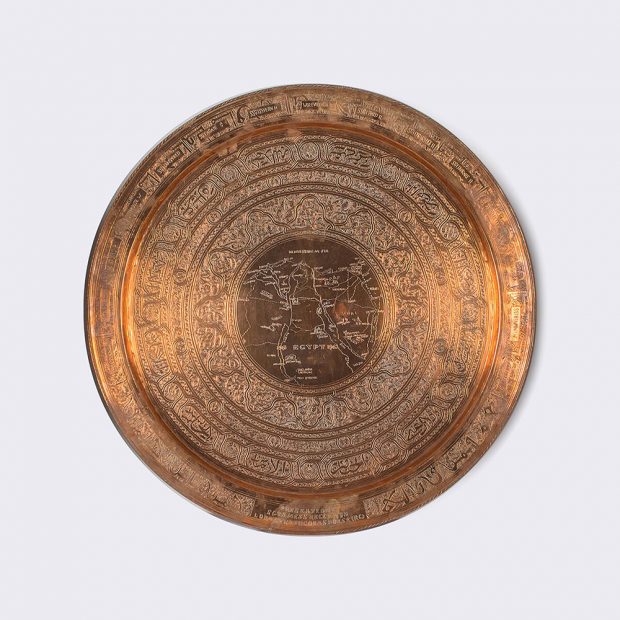 A larger shiny copper plate engraved with circles of design with a map in the middle.