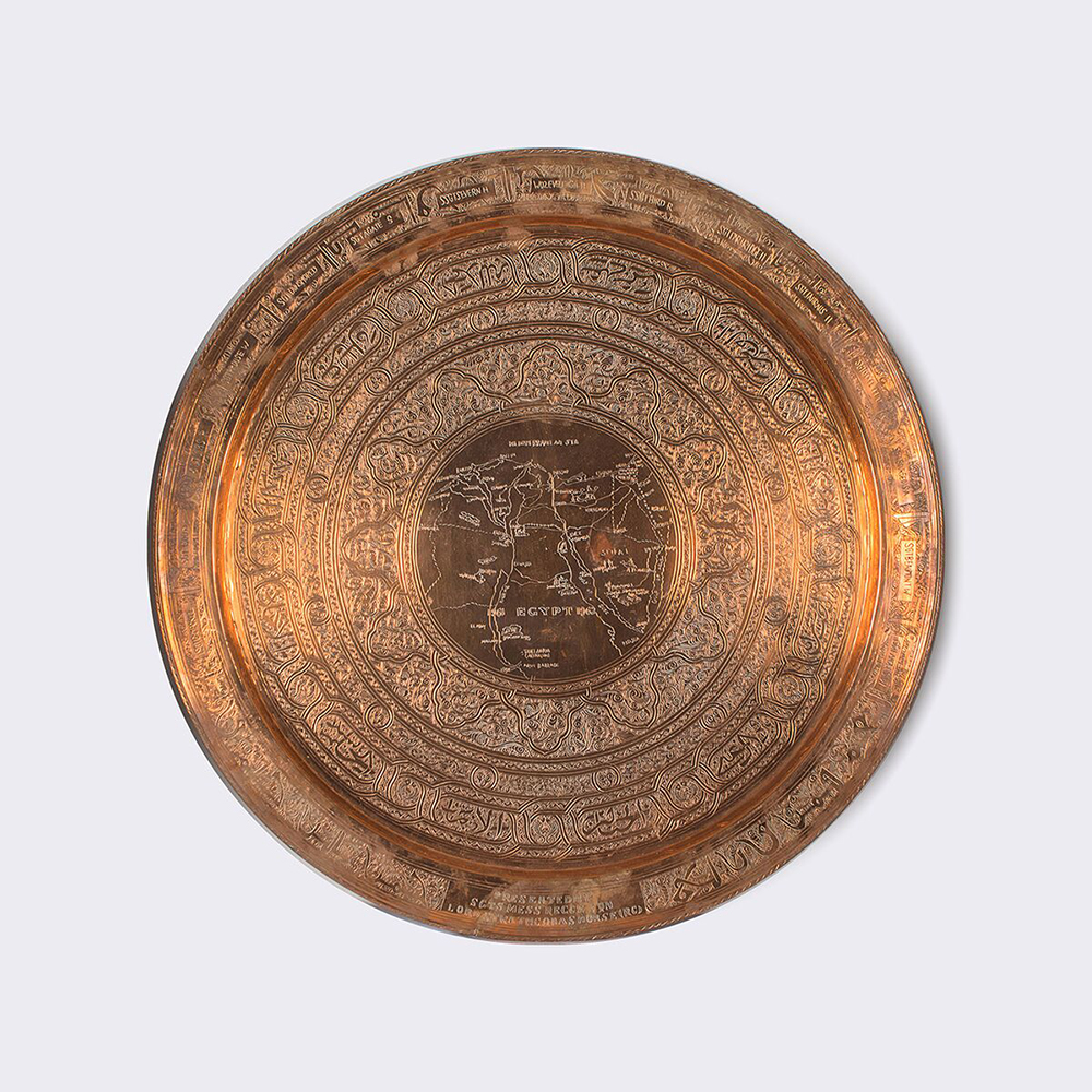 A larger shiny copper plate engraved with circles of design with a map in the middle.