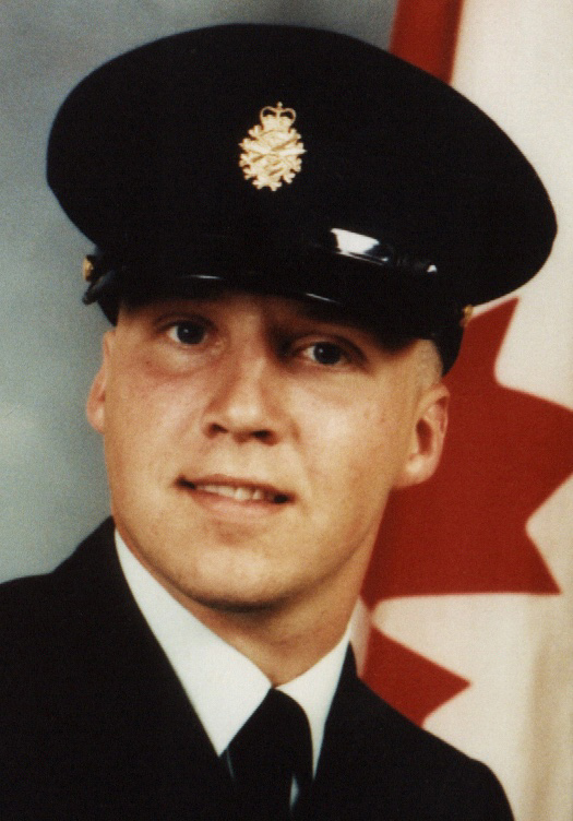 A color headshot of a smiling soldier in uniform before a Canadian flag.