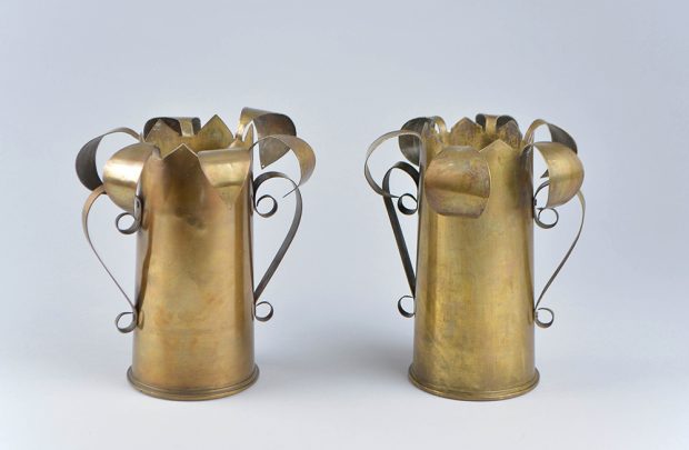 Two brass vases with cut and curled petals at top. The handles are made of cut and scrolled brass strips.