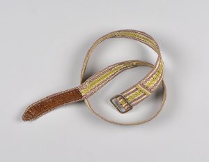 A colour photograph of a cotton woven belt with a leather end and metal clasp. Stripes of earth-toned colour run along its edges while a lime green stripe runs up the middle.