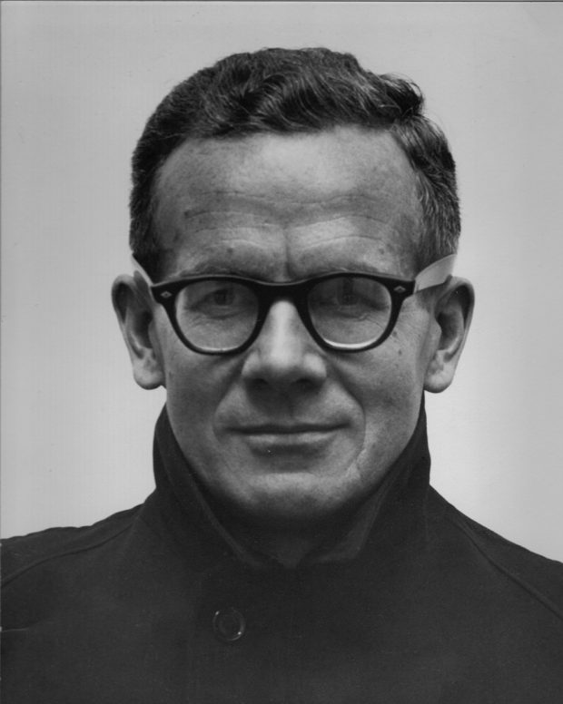 A black and white photograph professional headshot of a 40 year-old man with black-framed glasses staring at the camera with a slight smile.