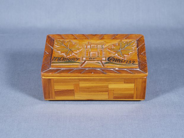 A handmade wooden box with lid embossed with a building flanked by maple leaves on both sides.