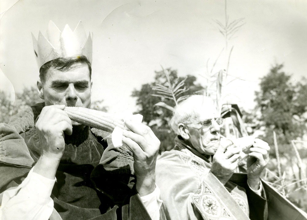 Black and white photograph of two men dressed in robes eating corn on the cob. The man on the left is 1950 Corn King Norman Morrow. The man on the right is 1949 Corn King Sam Stock.