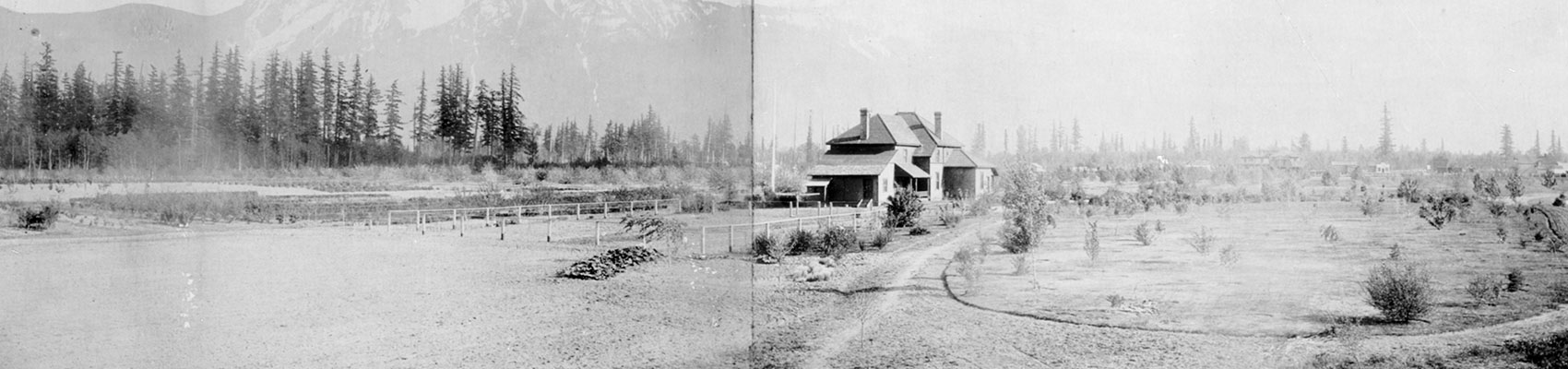 Black and white photograph of a house in a field. There are mountains in the background.