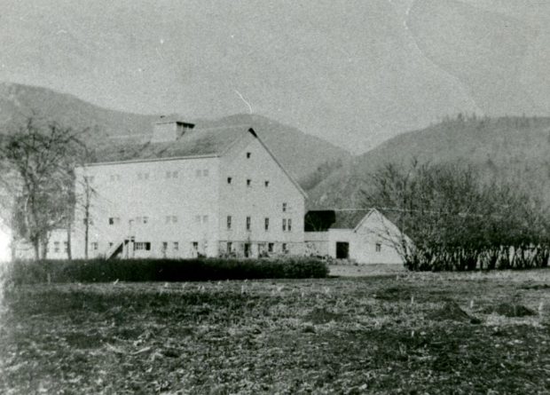 Black and white photograph of a stone barn surrounded by fields and mountains.