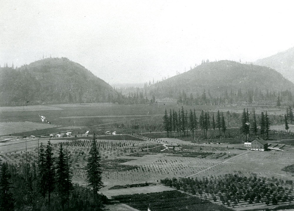 Black and white photograph of a barn, house, and fields with mountains in the background.