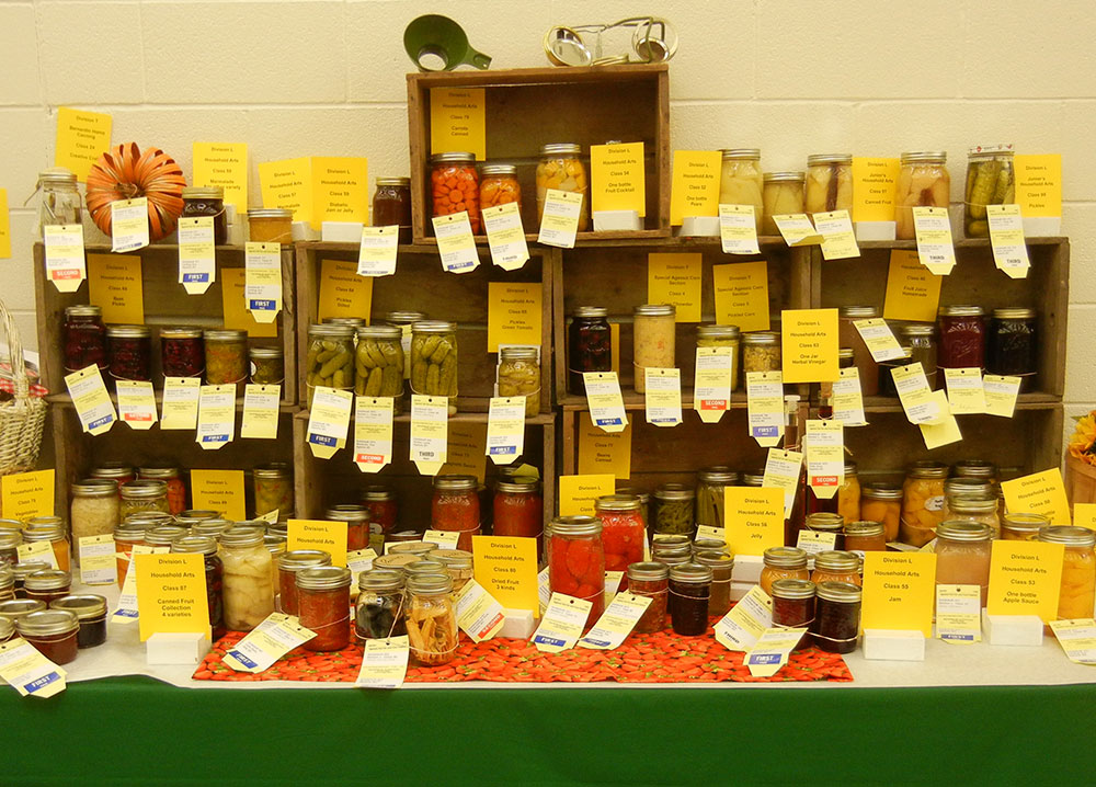 Colour photograph of mason jars of vegetables, fruit, and jam stacked in wooden crates.
