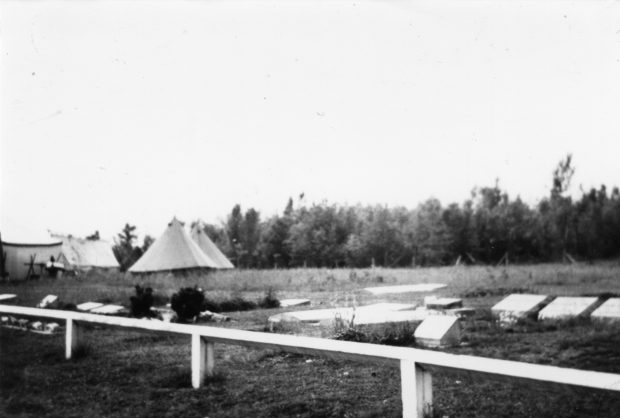 Black and white photograph of white tents next to a cemetery.