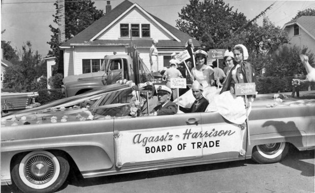 Black and white photograph of the Agassiz-Harrison Board of Trade car full of costumed adults in a parade, 1958.