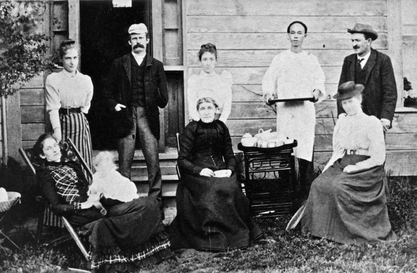 Black and white photograph of a family having tea outside their home. Included in the image is their Chinese manservant, 1891.