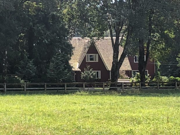 Colour photograph of a farm house with a field in the foreground.