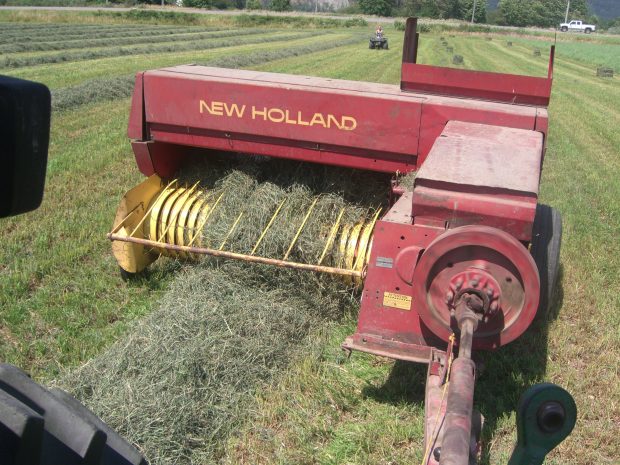 Colour photograph of a New Holland tractor baling hay.
