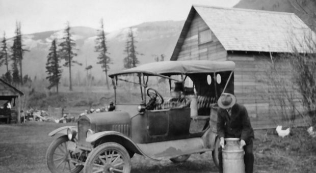 Black and white photograph of man loading milk cannisters into his Model T car.