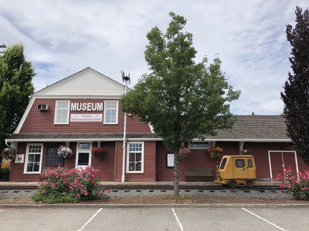 Colour photograph of a red and white barn-shaped historic train station, now the Agassiz-Harrison Museum and Visitor Information Centre.