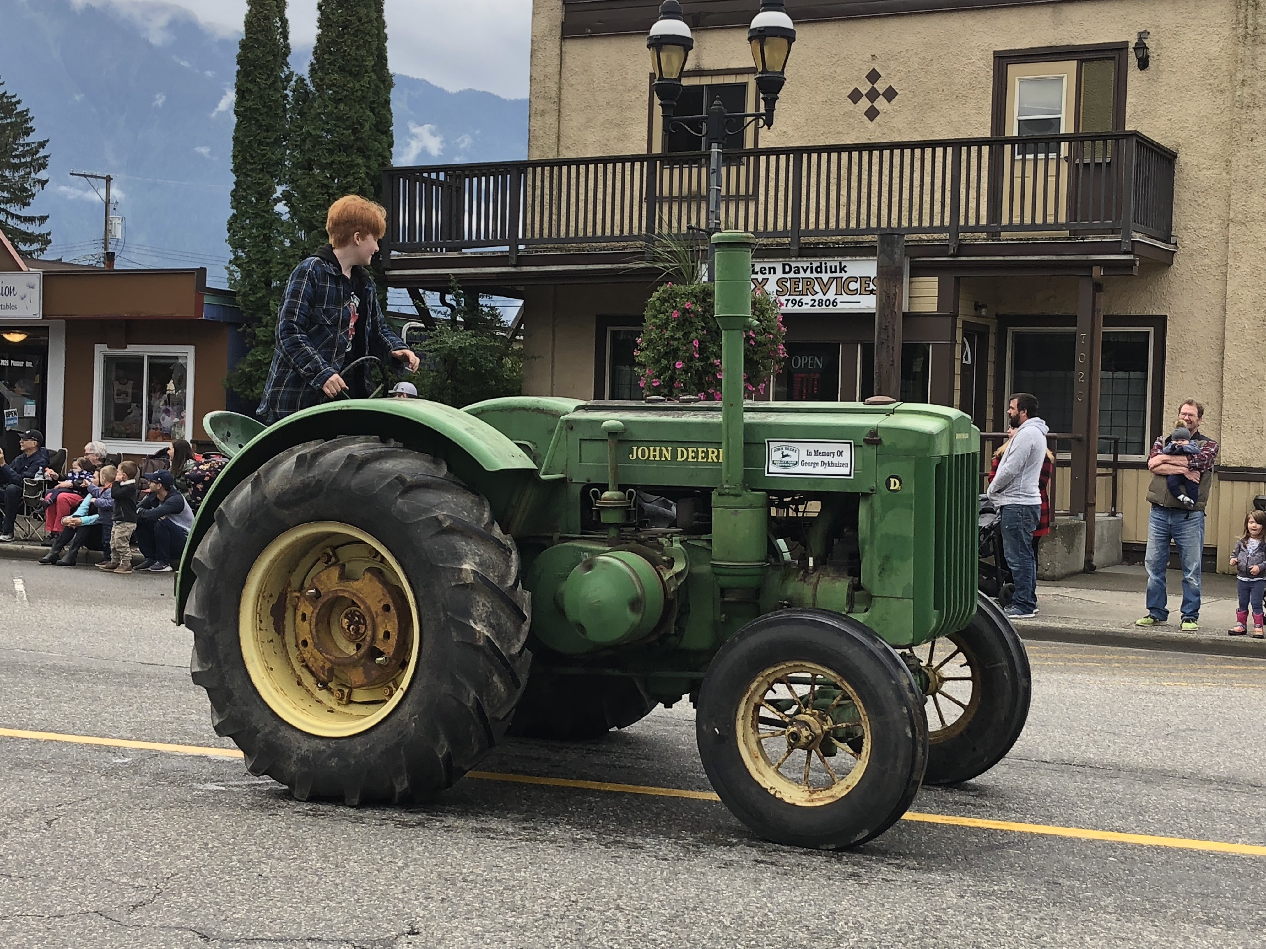Colour photograph of a teenager wearing a plaid jacket driving an antique John Deere tractor in a parade.