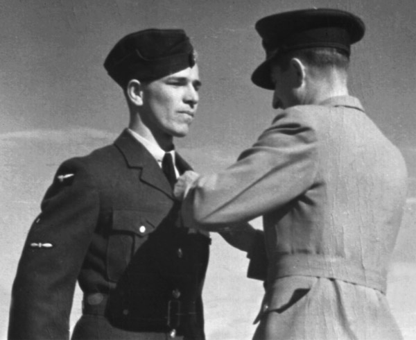 Black and white photo of two men in military uniform, one putting a pin on the other's chest.
