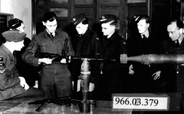 Group of men in military uniforms watching instructor demonstrating anti-aircraft gun