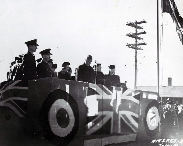 7 men and 4 women on a platform covered in flags