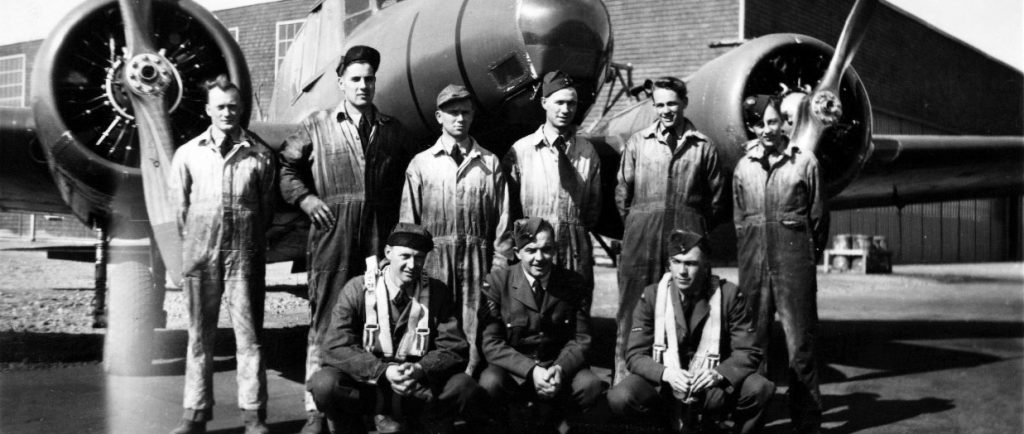 3 airmen and 6 mechanics in front of airplane and hangar