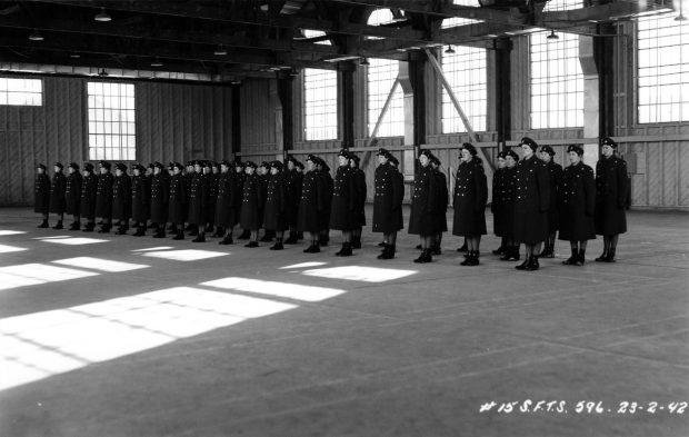 60 airwomen standing at attention in airplane hangar