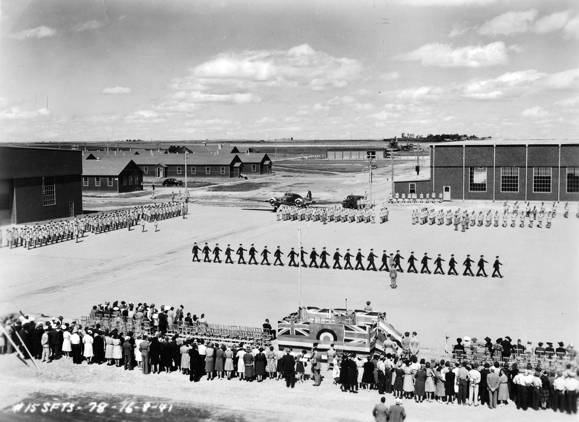 four groups of military men marching on parade square with crowd watching