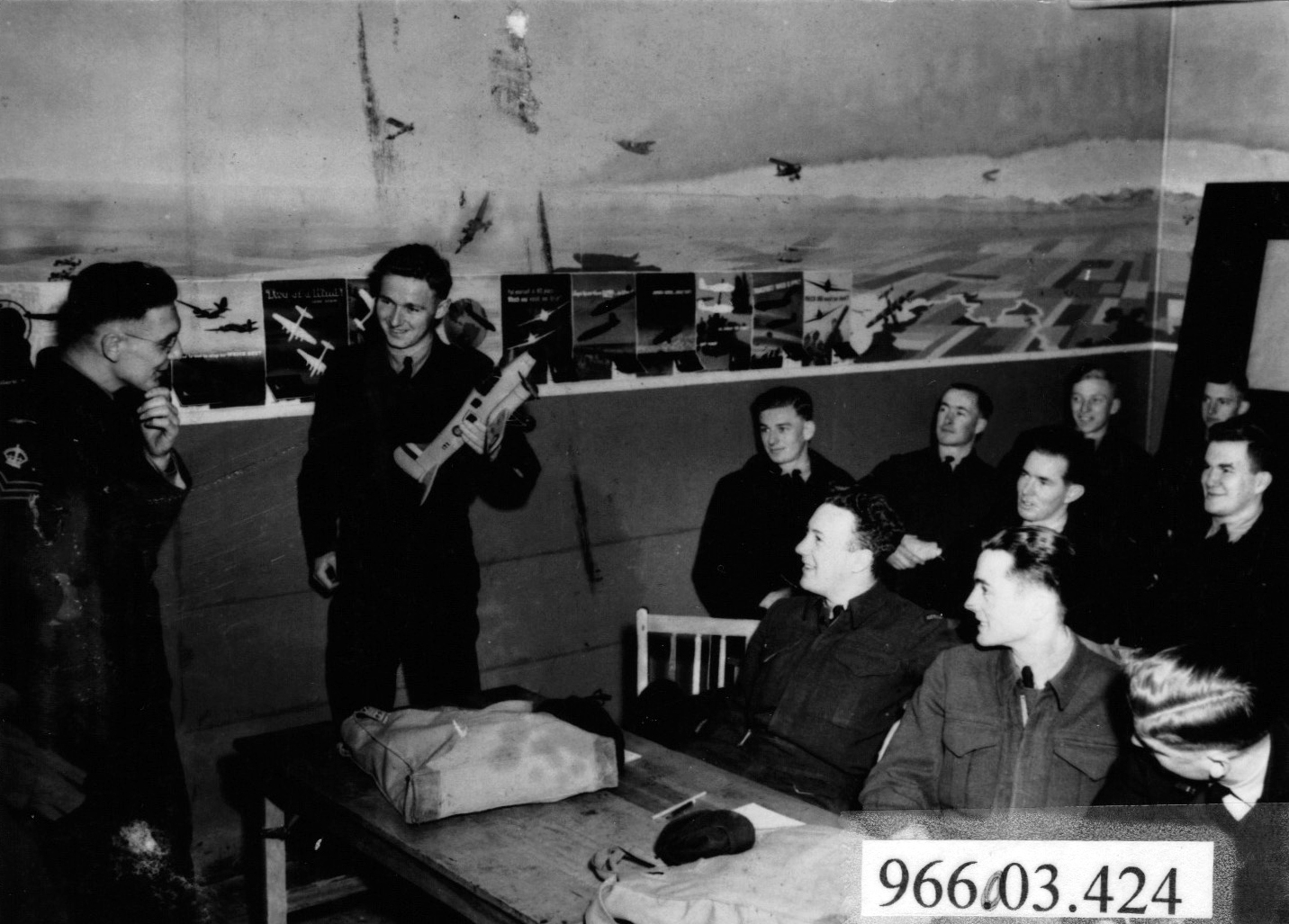 Airman holding model airplane in front of instructor and nine seated students