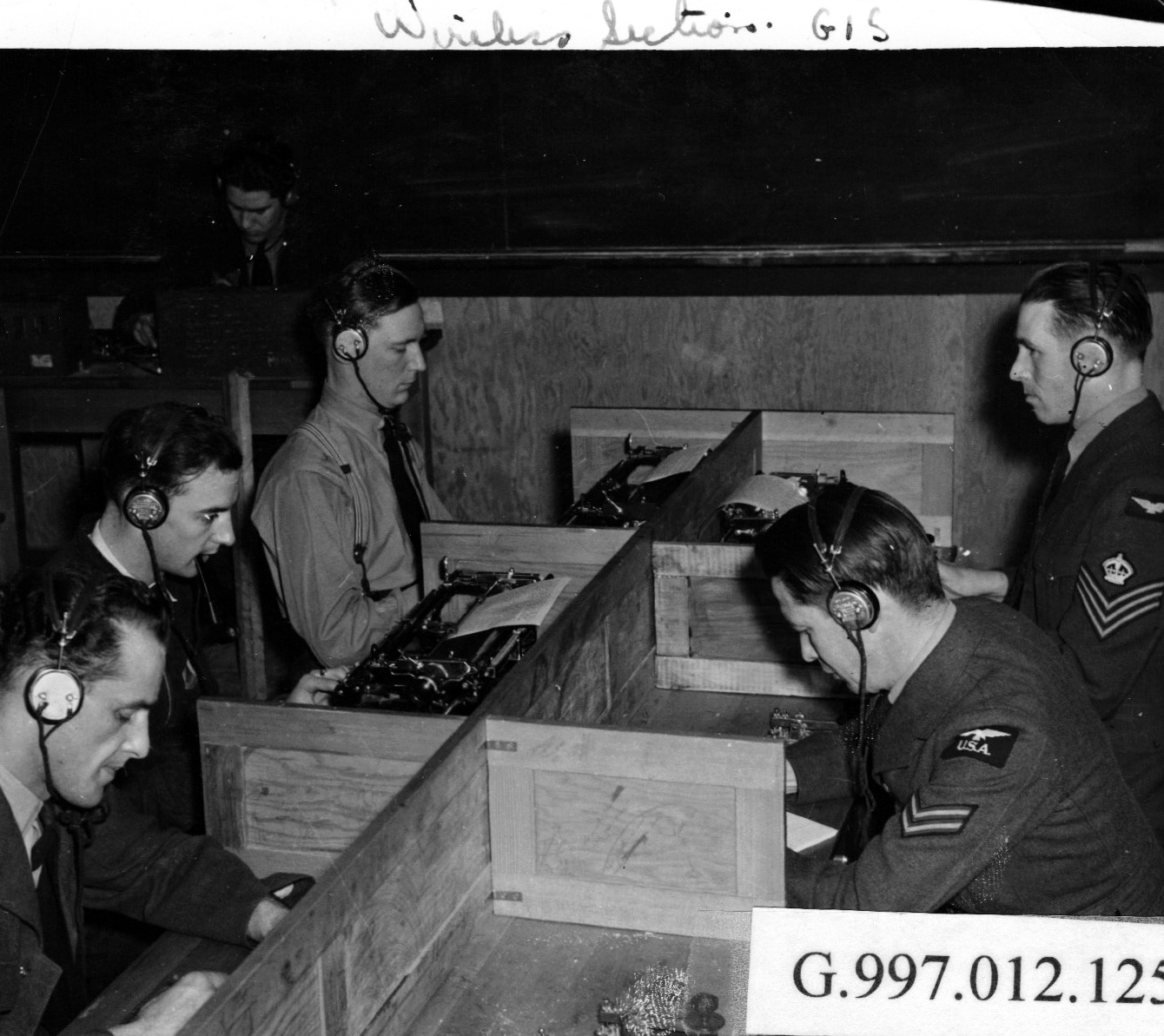 5 hommes en uniforme militaire équipés d’un casque d’écoute travaillant à un bureau