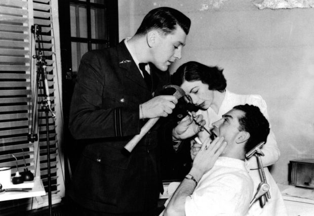 Military dentist working on male patient with female nurse assisting