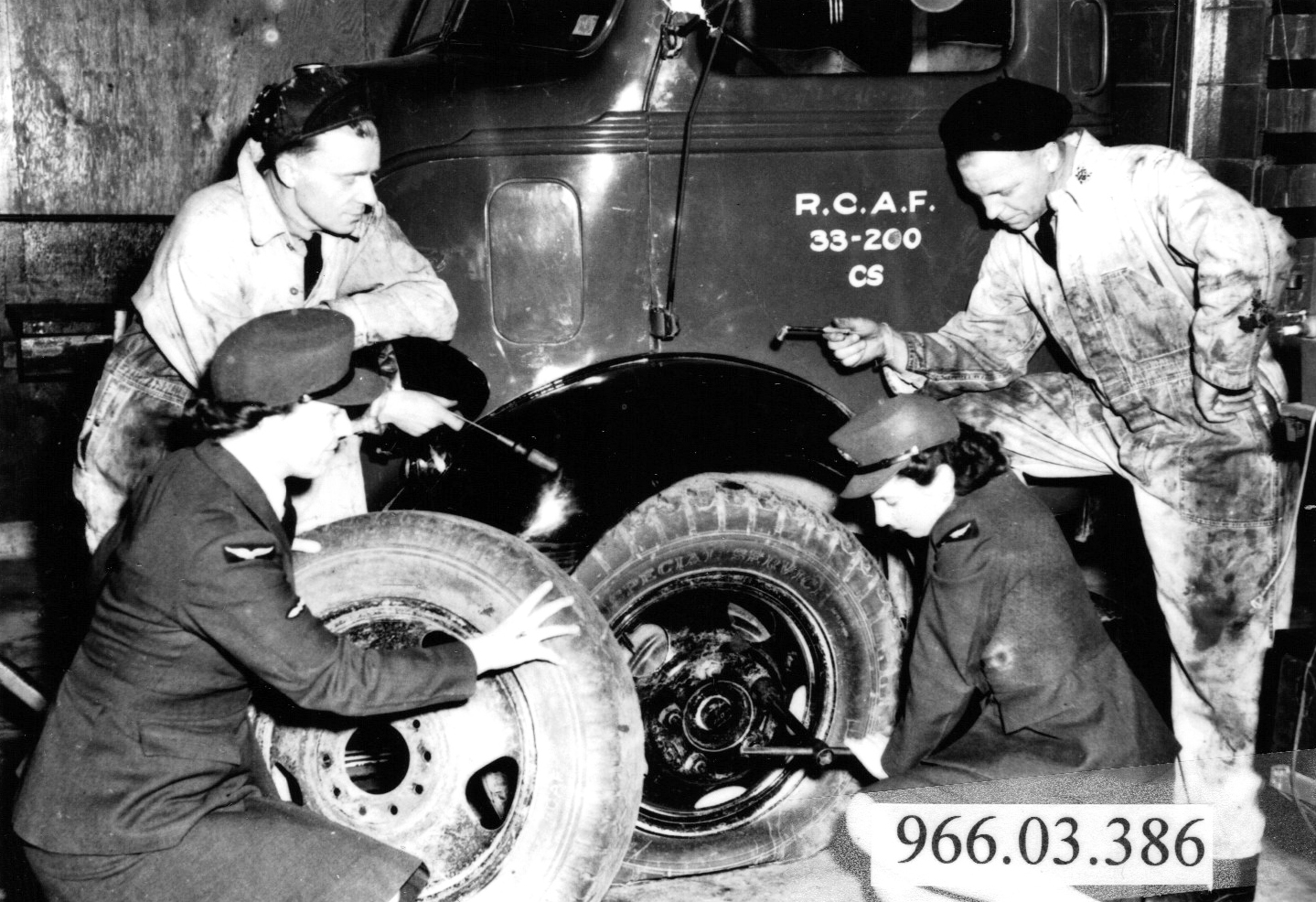 two airwomen changing truck tire with 2 male mechanics observing