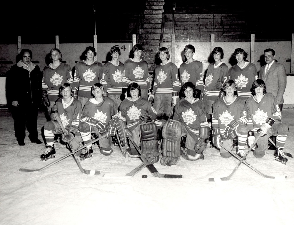 Photographie en noir et blanc sur laquelle on voit 14 garçons en tenue de hockey, dont la moitié se trouve à genoux sur une patinoire et l’autre moitié, debout derrière. Un homme se trouve de chaque côté des garçons.