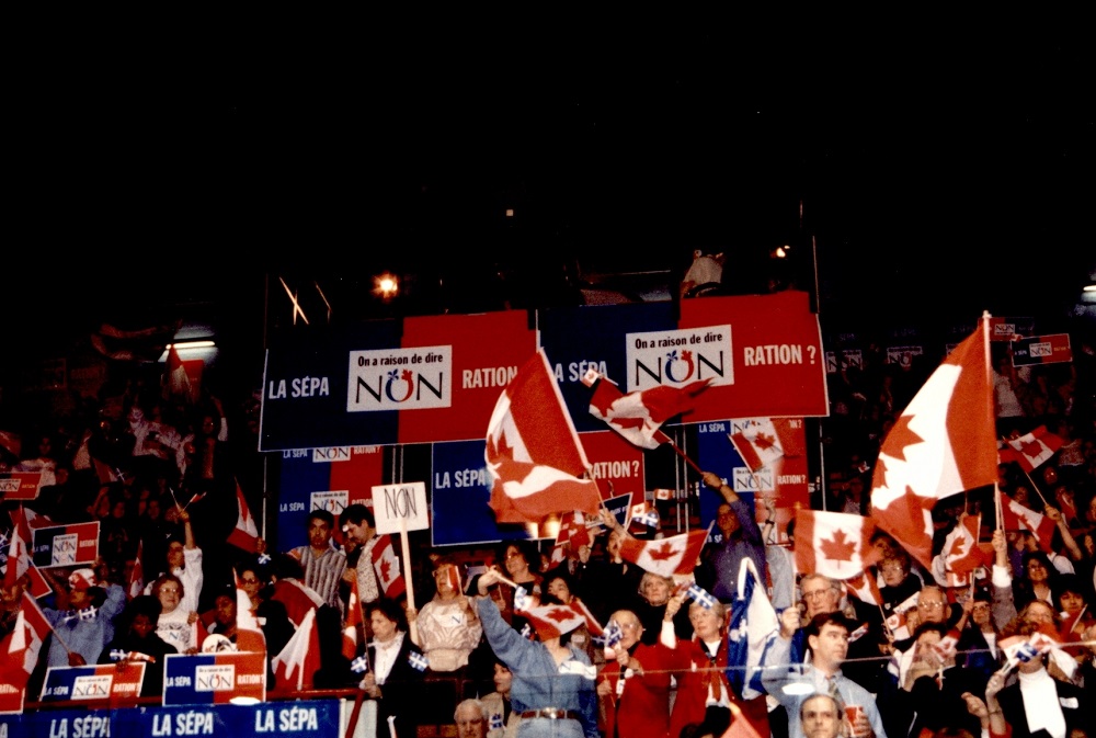 Colour photo showing a crowd of people in the stands, holding Canadian flags and placards.