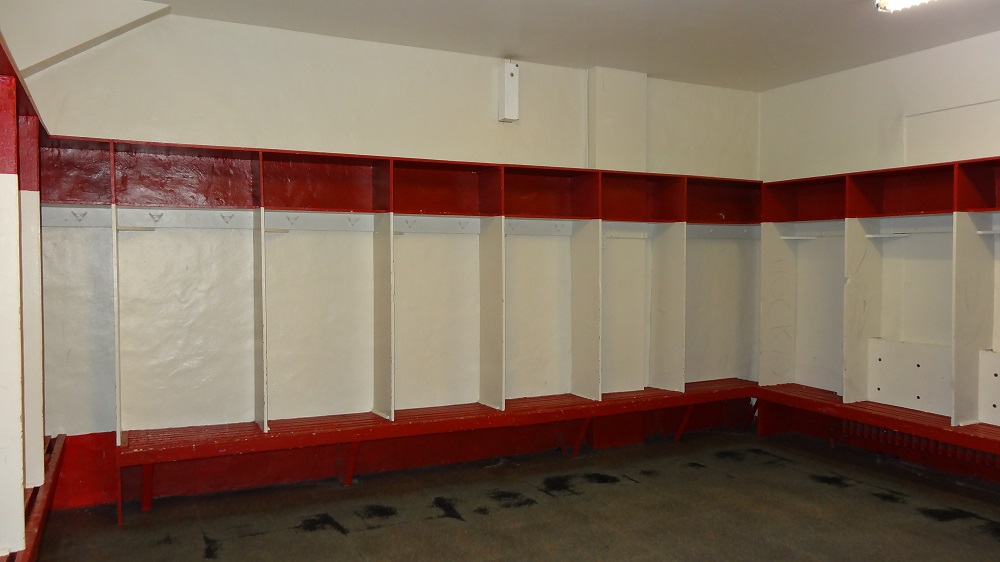 Colour photo showing a long red bench with several white vertical partitions on top. Each compartment also has a small red locker on top.