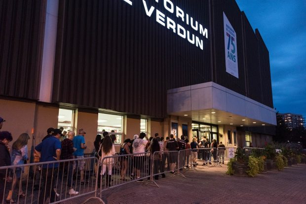 Colour photo of a line of people waiting to enter the main door of a building.