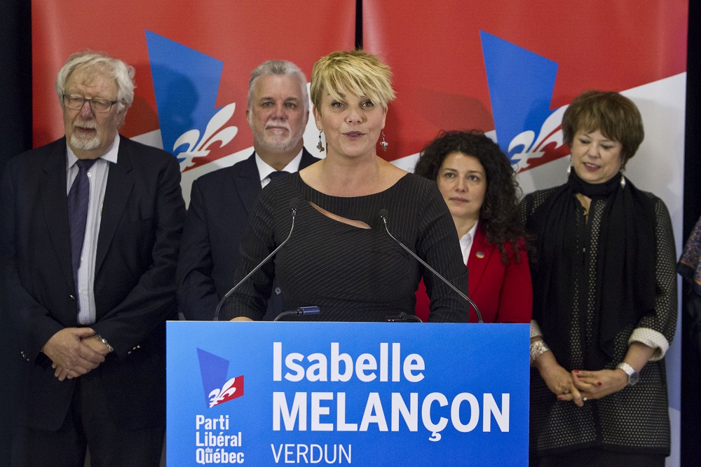 Colour photo showing a woman behind a podium. Four people, two men and two women, are standing behind her.