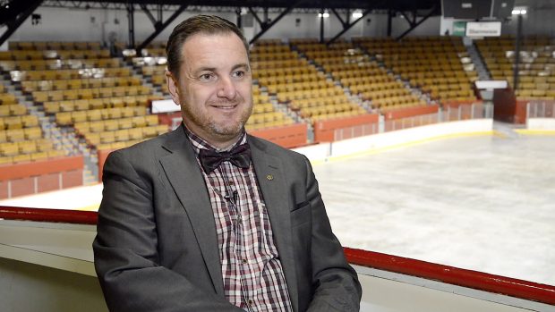 Colour photo of a man seated. Behind him, there are a skating rink and stands.