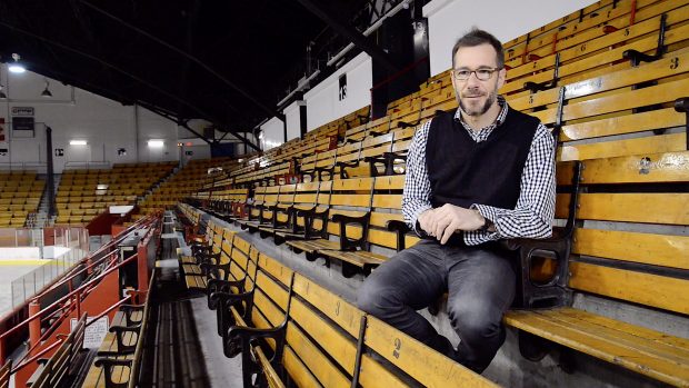 Colour photo of a man seating in a arena stand.