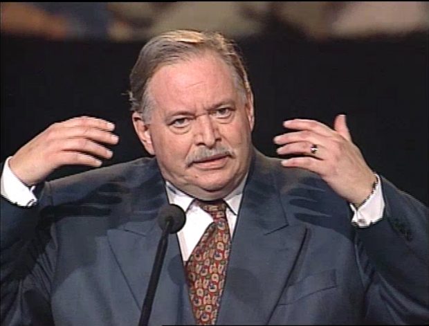 Colour photo of a man speaking at a microphone.