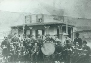 Une fanfare pose devant la maison du notaire Audet, elle-même devant la rivière Magog. 