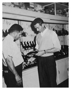 La photo présente Guy Papin, fils de Joseph III, avec un vendeur en 1964. Les deux hommes inspectent minutieusement une chaussure pour femme.