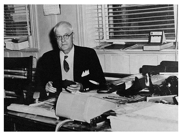 The picture shows Joseph Papin III in his office. He appears to be inspecting a pair of shoes.