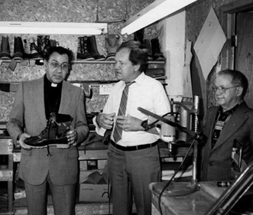 In this picture taken inside the factory, we see Georges Tétreault, the factory’s General Manager, accompanied on the left by Mgr. Bernard Hubert, bishop of the Saint-Jean diocese, and on the right by abbot Jean-Louis Yelle, the parish priest. Mgr. holds a boot in his hands while Mr. Tétreault appears to be providing explanations.